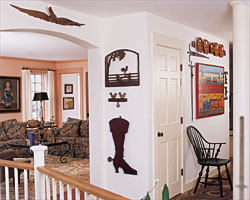 The most prominent object in the hallway is the 76-inch-high fireman’s helmet and horn weathervane with cast-iron flame directionals attributed to J.W. Fiske. Discovered on a Maine firehouse by Robert Bishop, it was exhibited in 1993 at the American Folk Art Museum in celebration of the opening of the Bishop wing. The couple commissioned the 1993 carving of the fireman, placed beside the firehouse weathervane, from Kentucky artist James Allen Bloomfield. Further down the hall is a pair of carved wooden boxers from the Barenholtz collection. They were given to toymaker Louis Marx, who, in 1938, used them as prototypes for his “Rock-em, Sock-em Robots” game. Needlework samplers from Mary Balch’s school in Providence, Rhode Island, Miss Patten’s School in Hartford, Connecticut, Newburyport’s Byfield Academy, and a number of schools in Pennsylvania, flank the carved 1987 hanging cabinet by Vermont artist Stephen Huneck (b. 1948). Below it is a painted blanket chest from 1830 by Joel Palmer of Fulton County, Pennsylvania, with initials for Henry Stoner. It descended in the Stoner family until purchased by Olde Hope Antiques and subsequently sold to the collectors. An 1890s horse silhouette weathervane is from Sam Herrup.