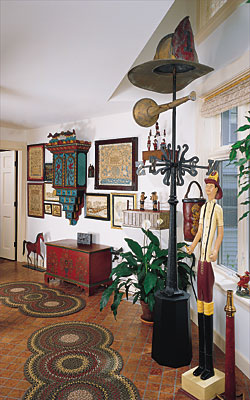 Hanging in the living room (to the left in the photograph) is a portrait of a young boy in a blue dress attributed by expert Don Walters to William Matthew Prior (1806-1873), circa 1845. Over the doorway is a carved “E. Pluribus Unum” eagle of 1875, attributed to John Haley Bellamy (1836–1914) of Portsmouth, New Hampshire, and Kittery, Maine. At 45 inches long, it has an unusually wide wingspan for a Bellamy. Ironware is mounted on the wall between the living room and hallway: a cast-iron barnyard scene from Pennsylvania hangs above a double rooster shooting target and a shoemaker’s trade sign. A Rhode Island continuous-arm Windsor in the hallway is situated under a monumental Jack Savitsky (1910–1991) painting, Reading Rail Road Miners’ Train, framed by early- 19th-century architectural iron hinges from dealer Rick Jorgensen. Mid- to late-19th-century redware plates from Olde Hope Antiques surmount the painting and hinges.