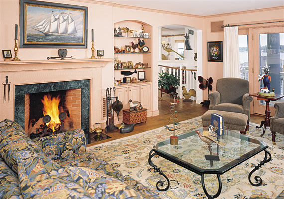 French doors open onto a deck from the living room. In front of the door a Connecticut candlestand with an elaborate base from Israel Sack, Inc. is juxtaposed with a whimsical contemporary carving by Brian McNutt. A 19th-century metal fireplace screen from North Carolina, in the form of a butterfly, sits beneath a rare floral painting of 1882 by almshouse artist John Rasmussen (1828–1895). The built-in cabinet houses an array of items including several portraits by Rufus Porter (1792–1884); transfer jugs and children’s cups; Lehn ware; and a Reber rooster. A Pennsylvania miniature blanket chest supports a 1940 pintail drake by George Barto; a 1950 carved mallard by Robert Leibensperger is on the floor. The ship John J. Hanson, painted by S.F.M. Badger (1873–1919), circa 1885, is displayed over the mantel, which supports an 1880 cast-iron heart-shaped rope maker. A rare “Schtockschnitzler” Simmons (1885–1910). Pennsylvania bird tree with nine birds is placed on the glass table. Also on the table is a 19th-century iron gate weight in the form of a dove. The “Cinderella Whistle Book” is by contemporary carver Constance Roberts of California.