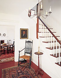 In the hall hangs a portrait of a dashing New England sea captain by Amsterdam port painter Carolus Delin (1756-1818) who painted many visiting American mariners to his city. The tin chandelier hangs above a bold Connecticut banister back chair.
