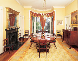 Click Here for Enlarged View The oval mahogany table, that seats from eight to twenty-two people, and the sideboard, were probably made in New York. Though they're quite delicate, our couple uses the Boston klismos chairs, 1820, and another set of chairs from Philadelphia, 1825, for seating when company arrives. A carved mahogany Restauration tilt-top center table, 1825-1830, from Boston or Salem, nestles into the bay window, which was added shortly after the house was built and makes a picturesque breakfast nook. A Charles Herbert Woodbury (1864-1940) sketch depicting the Shaw Memorial to the Massachusetts 54th Regiment hangs on the far wall. The 54th was one of the first formal units of the U.S. Army to be made up entirely of African American men (apart from the officers). Woodbury is best known as a marine painter.