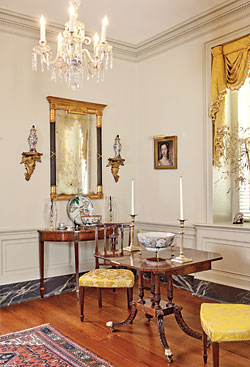 A rare, circa-1800–1810 card table attributed to Charleston is one of the couple’s finest pieces. The late John Bivens, a Charleston furniture scholar and private consultant/dealer, felt that, though having elements from other style centers, the details and carving were closely associated with locally made furniture, with decorative elements also relating to Charleston interiors. Conservation of the table revealed that it was made as one of a pair. The table is flanked by a pair of New York side chairs, circa 1800. A Federal looking glass with ebonized reeded columns hangs above a Federal card table. The portrait of a woman is attributed to John Wollaston (1710–1775); the husband purchased this at an antiques show as a gift for his wife.