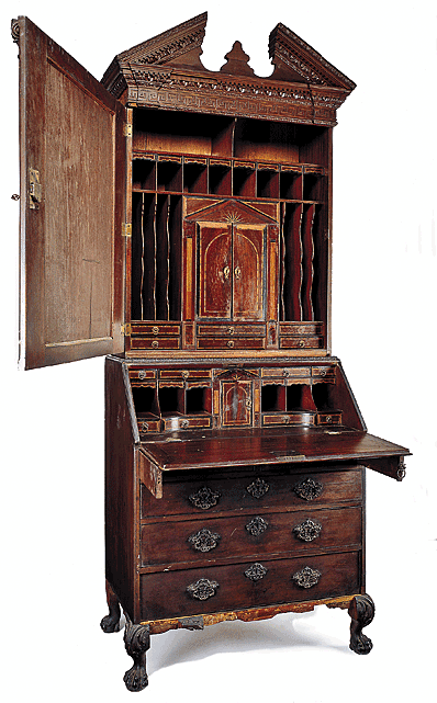 Fig. 10: Bureau bookcase, possibly by John Channon, London, England, mid-eighteenth century. 39 x 22 x 96 in. Original brasses and escutcheons. Donation of Charles H. Drayton. Courtesy, Drayton Hall, a historic site of the National Trust for Historic Preservation. Currently housed within the collections of the Colonial Williamsburg Foundation, Williamsburg, Virginia. Photography courtesy George Williams.  Constructed in two parts, the upper section of this rare example is topped with a broken pediment with a flush-mounted plinth in the center. The tympanum and frieze display a series of moldings composed of egg-and-dart, dentil, foliate, and Greek key motifs. The pediment surmounts an upper case with a single door flanked by two engaged Corinthian pilasters. The lower case consists of two-over-three graduated drawers below a fall board, decorated with cockbeading and veneered in mahogany. All associated rococo brasses and escutcheons are original. The desk interior exhibits a temple form prospect enclosing a compartment having an inlaid floor and a mirrored interior. The prospect assembly is in two parts, both removable. The upper portion is a drawer, the lower is a dovetailed case containing three small secret drawers at the rear. The prospect is flanked by projecting curvilinear sections containing pigeonholes, small drawers, and valance drawers. The drawers are veneered, inlaid, and crossbanded. The associated base repeats the leaf-carved molding of the pediment on carved ball-and-claw feet.