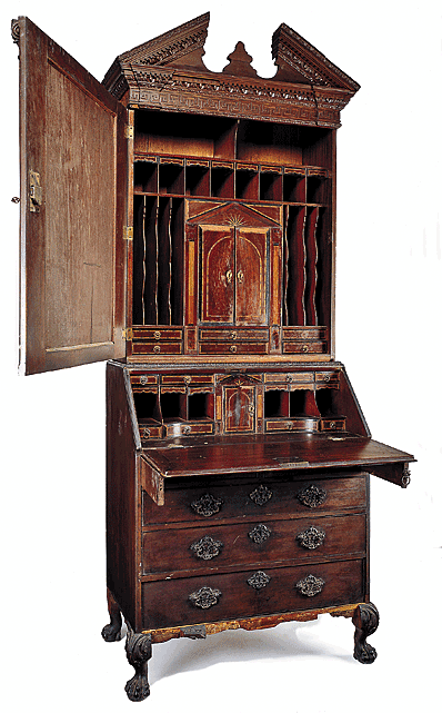 Fig. 10: Bureau bookcase, possibly by John Channon, London, England, mid-eighteenth century. 39 x 22 x 96 in. Original brasses and escutcheons. Donation of Charles H. Drayton. Courtesy, Drayton Hall, a historic site of the National Trust for Historic Preservation. Currently housed within the collections of the Colonial Williamsburg Foundation, Williamsburg, Virginia. Photography courtesy George Williams. Constructed in two parts, the upper section of this rare example is topped with a broken pediment with a flush-mounted plinth in the center. The tympanum and frieze display a series of moldings composed of egg-and-dart, dentil, foliate, and Greek key motifs. The pediment surmounts an upper case with a single door flanked by two engaged Corinthian pilasters. The lower case consists of two-over-three graduated drawers below a fall board, decorated with cockbeading and veneered in mahogany. All associated rococo brasses and escutcheons are original. The desk interior exhibits a temple form prospect enclosing a compartment having an inlaid floor and a mirrored interior. The prospect assembly is in two parts, both removable. The upper portion is a drawer, the lower is a dovetailed case containing three small secret drawers at the rear. The prospect is flanked by projecting curvilinear sections containing pigeonholes, small drawers, and valance drawers. The drawers are veneered, inlaid, and crossbanded. The associated base repeats the leaf-carved molding of the pediment on carved ball-and-claw feet.